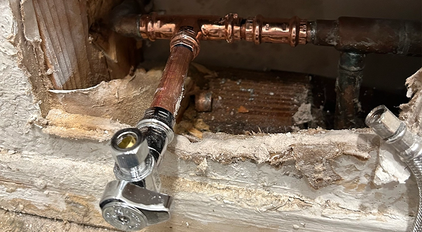 Copper plumbing pipes with visible fittings and a silver valve in a wall.